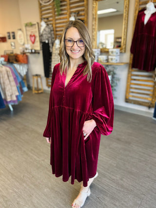 Woman wearing burgundy velvet babydoll dress with long sleeves in clothing boutique setting