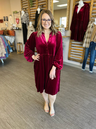 Woman wearing burgundy velvet babydoll dress with long sleeves in clothing boutique setting