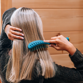 Person brushing long blonde hair with a TELETIES vented hair brush from behind.