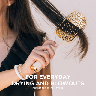 Woman brushing long dark hair with a gold and cream vented hair brush.