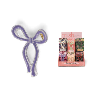 Purple bow-shaped hair clip displayed next to colorful product packaging with multiple design options.