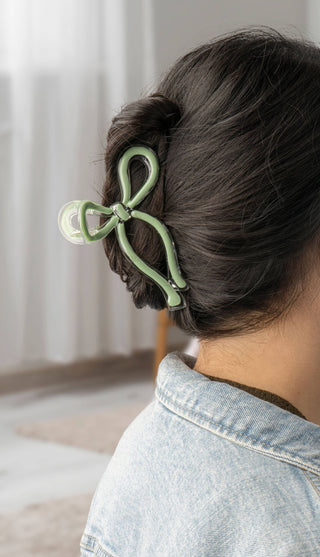 Person wearing a sage green bow-shaped hair clip holding up a messy bun hairstyle.