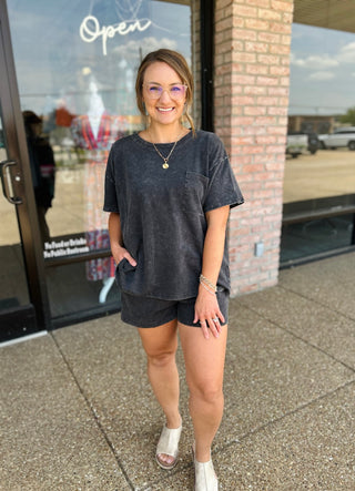 Woman wearing a relaxed matching oversized tee and shorts set with mule sandals outside boutique.