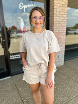 Woman wearing a matching relaxed short sleeve top and drawstring shorts set, standing outside a boutique.