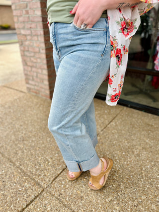 Woman wearing light wash high-rise wide leg jeans with rolled cuffs and brown heeled sandals.