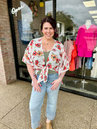 Woman wearing floral kimono top and high-rise wide leg jeans standing outside clothing boutique storefront.