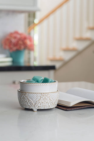 Vintage white ceramic fragrance warmer with intricate pattern sits on counter next to open book