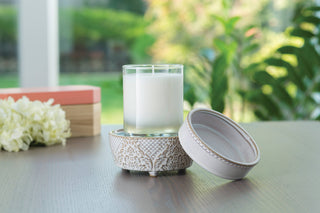Vintage white ceramic fragrance warmer with decorative pattern on wooden table with candle and flowers