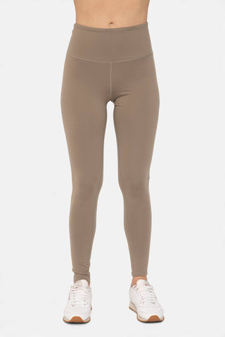 Woman wearing high-waisted athletic leggings with tummy control panel and white sneakers on neutral background.