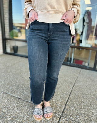 Woman wearing high-rise cropped flare jeans with frayed hem, paired with beige sweatshirt and sandals.