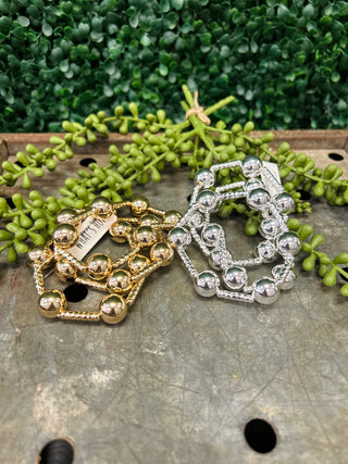Water resistant beaded bracelets in metallic finishes displayed on wooden surface with green plants