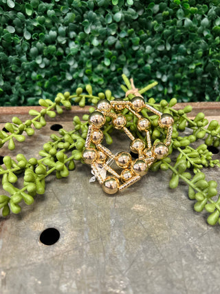 Gold beaded water resistant bracelet displayed on wooden surface with green succulent plants in background.