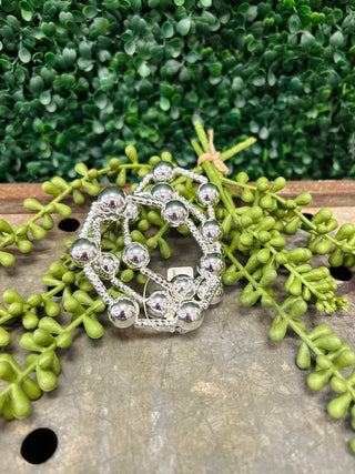 Water resistant beaded bracelets with metallic spheres displayed on wooden surface with green succulent plants.