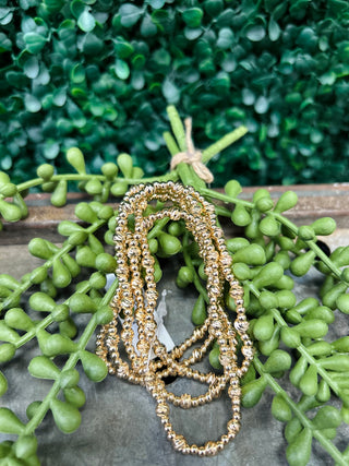 Water resistant beaded bracelets in gold tones displayed on wooden surface with green succulent plants