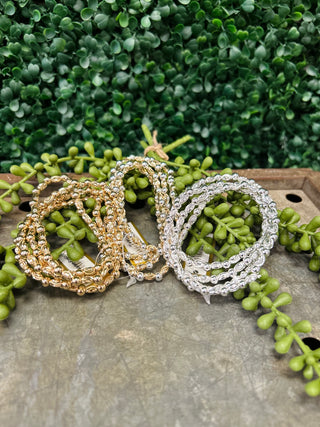 Water resistant textured oval beaded bracelets in metallic finishes displayed on wooden surface with green plants.