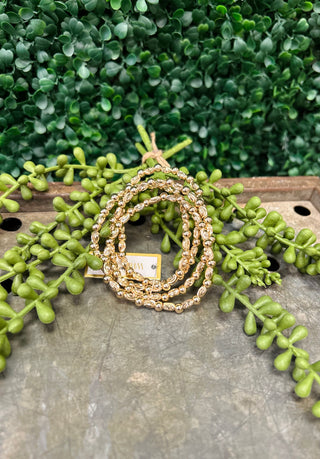 Gold textured oval beaded bracelets displayed on wooden surface with green succulent plants in background.