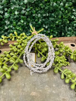 Silver textured oval beaded bracelets displayed on wooden surface with green succulent plants in background.