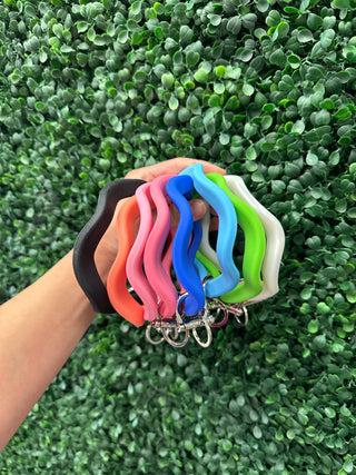 Hand holding colorful silicone wave-shaped keychains with metal rings against green foliage background