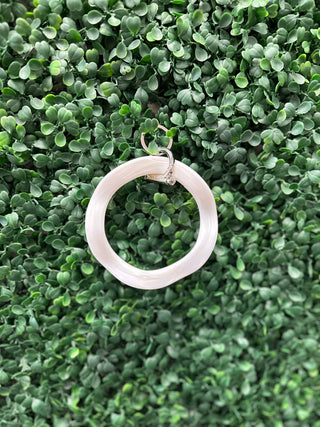 Pink wavy circular keyring with metal clasp displayed against green leafy plant background.