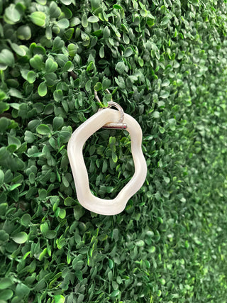 Clear acrylic wavey-shaped keyring with metal clasp displayed on green foliage background.