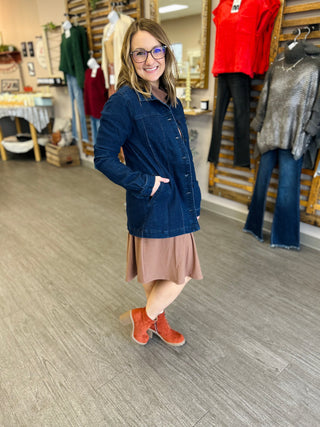 Woman wearing dark denim jacket over pink dress with orange boots in clothing store