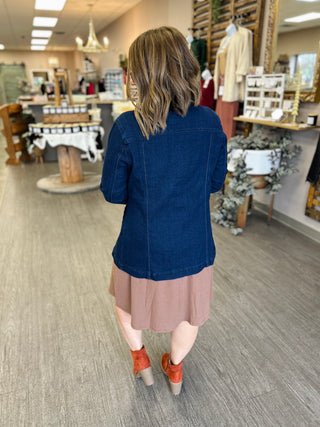 Woman wearing dark denim jacket and pink skirt walking through retail store, shown from behind.