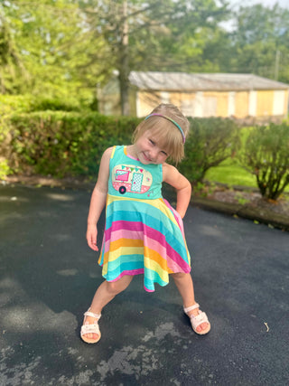 Young girl wearing colorful striped sleeveless dress with camper van graphic, posing on driveway outdoors