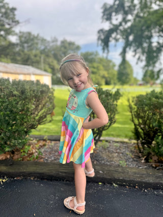 Young girl wearing colorful striped sleeveless dress posing outdoors in residential neighborhood setting.