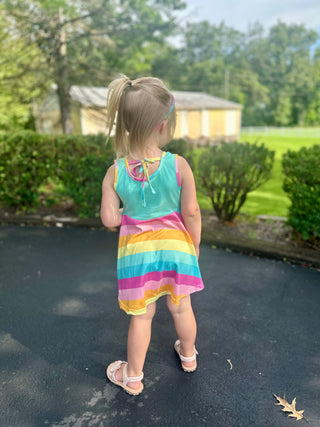 Young girl wearing colorful striped sleeveless dress walking on pavement in residential neighborhood setting.