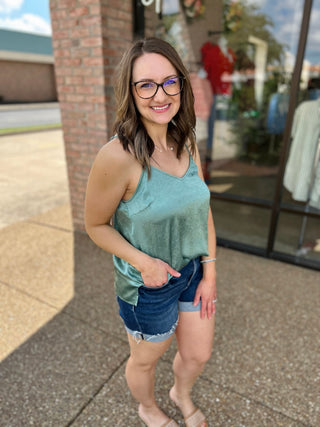 Woman wearing mint green sleeveless cami top with denim shorts, standing outdoors smiling.