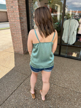 Woman wearing sage green camisole and denim shorts walking past storefront window