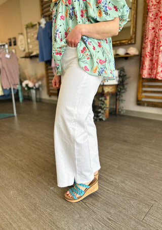Woman wearing white high-rise cropped wide leg jeans with floral top and platform sandals in boutique setting.