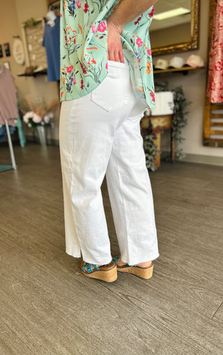 Woman wearing white high-rise cropped wide leg jeans with floral top and platform sandals in boutique setting.