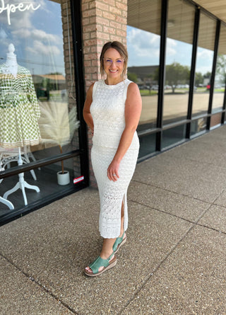 Woman wearing white crochet midi dress with side slit and green sandals outside storefront