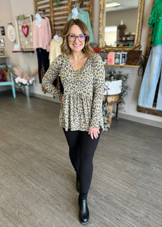Woman wearing leopard print babydoll top with black leggings and boots in boutique setting