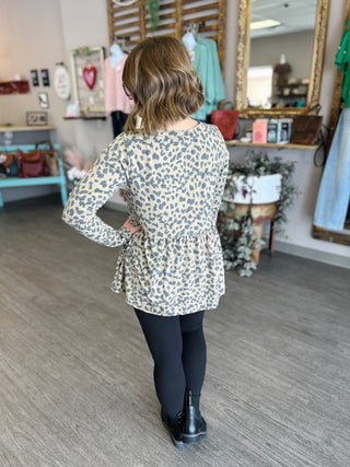 Woman wearing leopard print babydoll top with long sleeves and dark jeans, shown from behind in boutique setting.