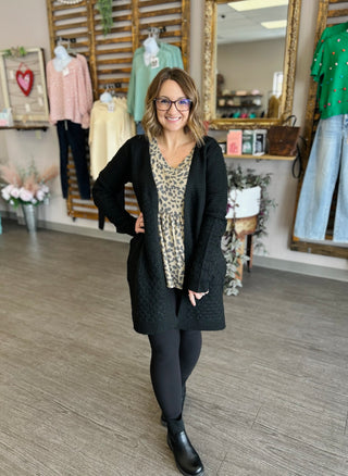 Woman wearing leopard print babydoll top with black cardigan and leggings in boutique setting