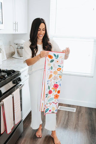 Woman in white kitchen holding colorful floral patterned kitchen towel with coral trim
