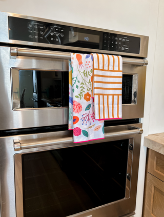 Colorful floral and striped kitchen towels hanging on stainless steel oven handle in modern kitchen