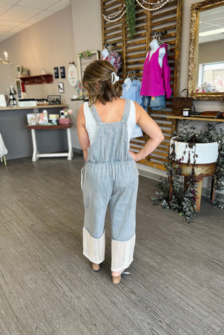 Woman wearing denim overalls with white lace hem detail in boutique clothing store setting.