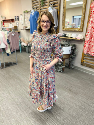 Woman wearing floral patterned ruffle dress with three-quarter sleeves standing in clothing boutique