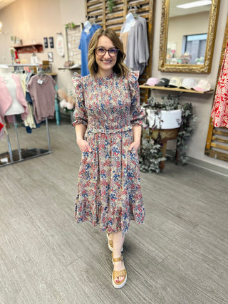 Woman wearing a floral print midi dress with ruffles and pockets in a boutique setting.