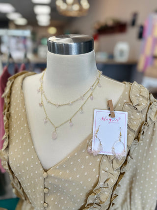 Mannequin wearing layered gold necklaces with pink stones and matching earrings over beige polka dot blouse in boutique se...
