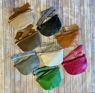 Nine colorful woven bum bags with adjustable straps arranged in a circle on wooden background.
