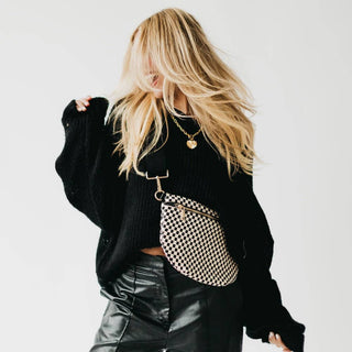 Woman wearing black sweater with checkered crossbody bum bag, hair in motion against white background.