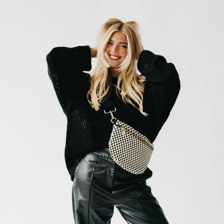 Woman wearing black sweater and leather pants with black and white checkered crossbody bum bag.