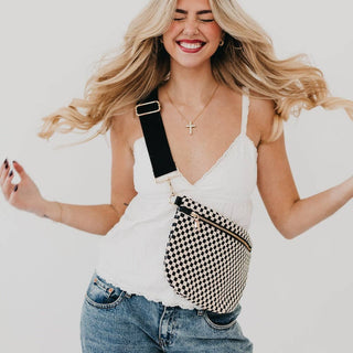 Woman wearing checkered crossbody fanny pack with white top and jeans, smiling with flowing blonde hair