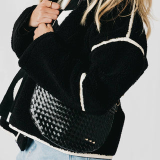 Woman wearing black hoodie carrying black woven crossbody bum bag with adjustable strap