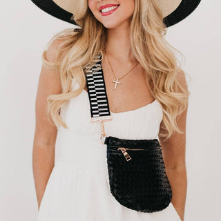 Woman wearing black woven bum bag with striped strap across white dress and sun hat