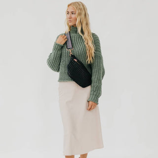 Woman wearing green knit sweater and beige skirt with black woven crossbody bum bag